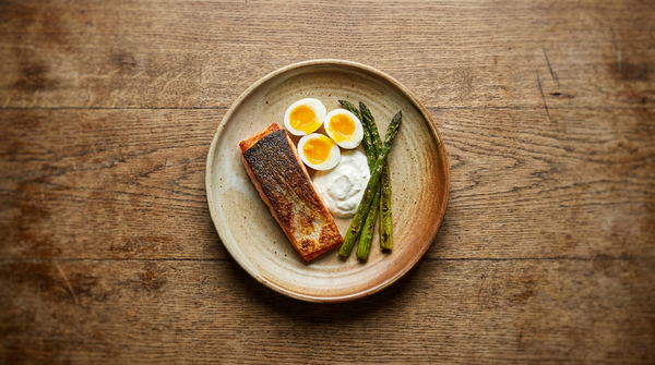 Small plate with salmon, soft-boiled eggs, Greek yogurt and asparagus surrounded by negative space, showing nutrient density over volume